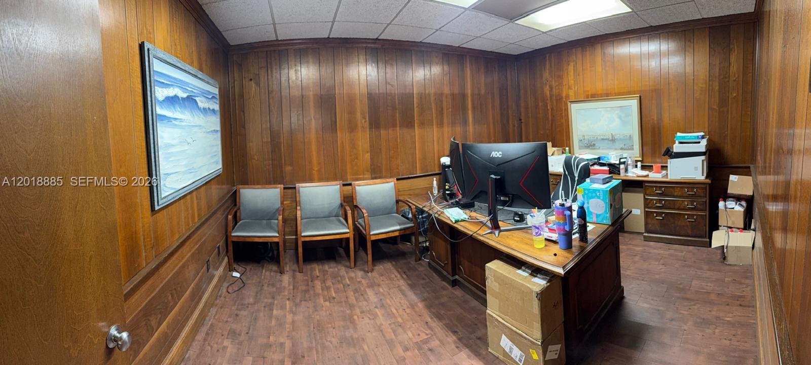 An office features wood-paneled walls, a desk with a computer monitor, and three guest chairs — PARKLAND, FL