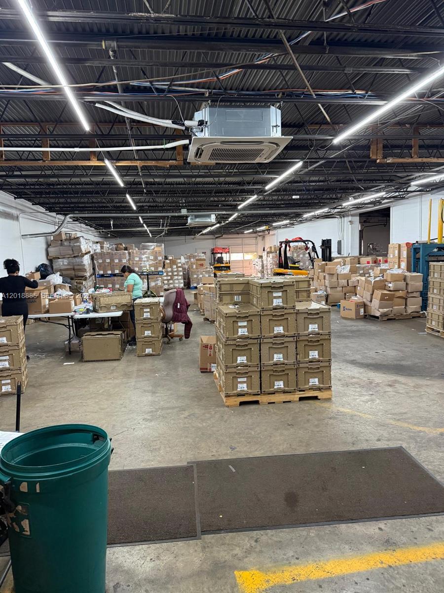 A warehouse interior features stacks of cardboard boxes, a packing station, and industrial lighting — PARKLAND, FL