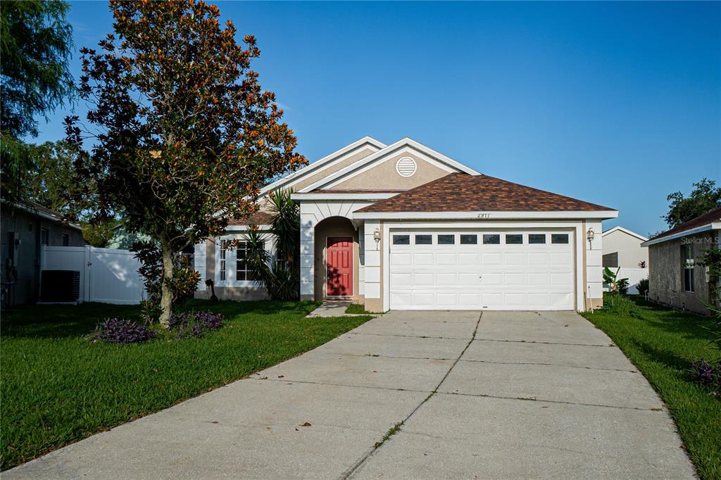 A single-story house with a white garage, red front door, and a large tree — 2917 WILSHIRE ROAD, CLERMONT, FL
