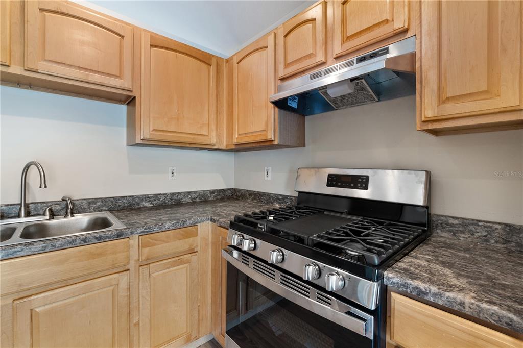 A kitchen features light wood cabinets, a stainless steel gas range, and dark laminate countertops — 2917 WILSHIRE ROAD, CLERMONT, FL