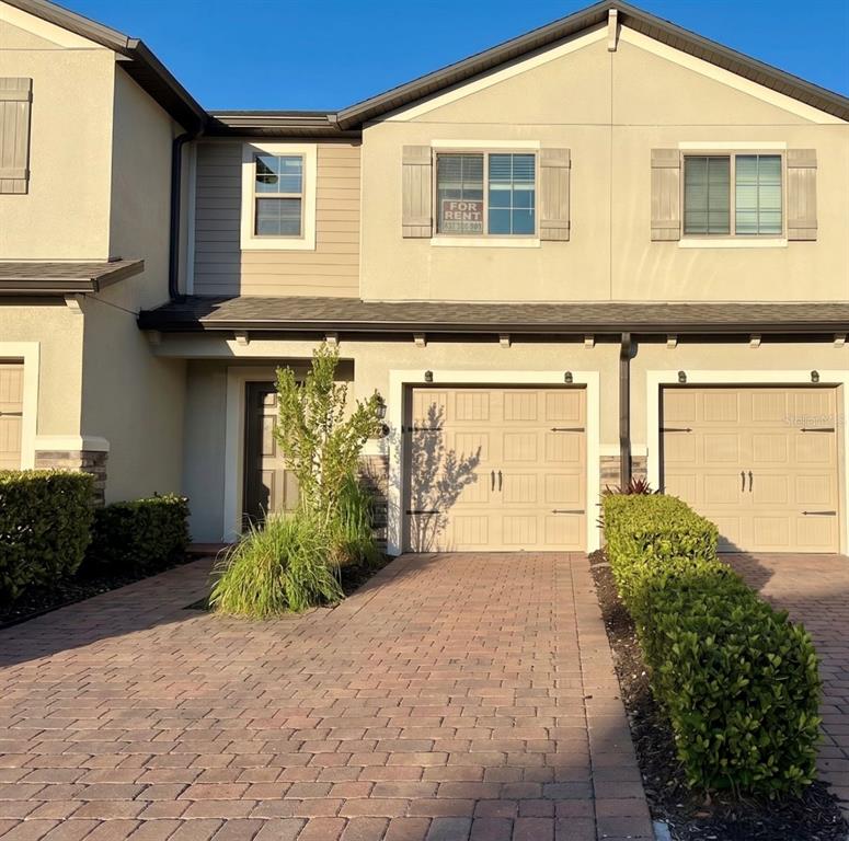 A two-story townhouse exterior features a brick driveway, two garage doors, and a for-rent sign — 1031 FLOWING TIDE DRIVE, ORLANDO, FL