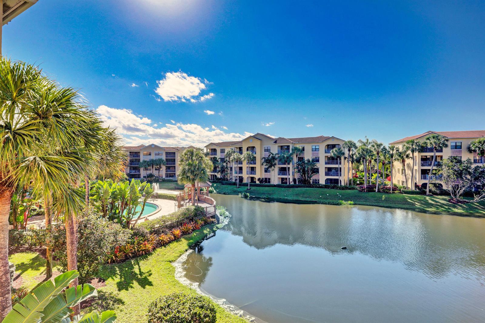 An exterior view of apartment buildings overlooking a lake with a pool and palm trees — 800 Uno Lago Drive # 305, Juno Beach FL 33408, JUNO BEACH, FL