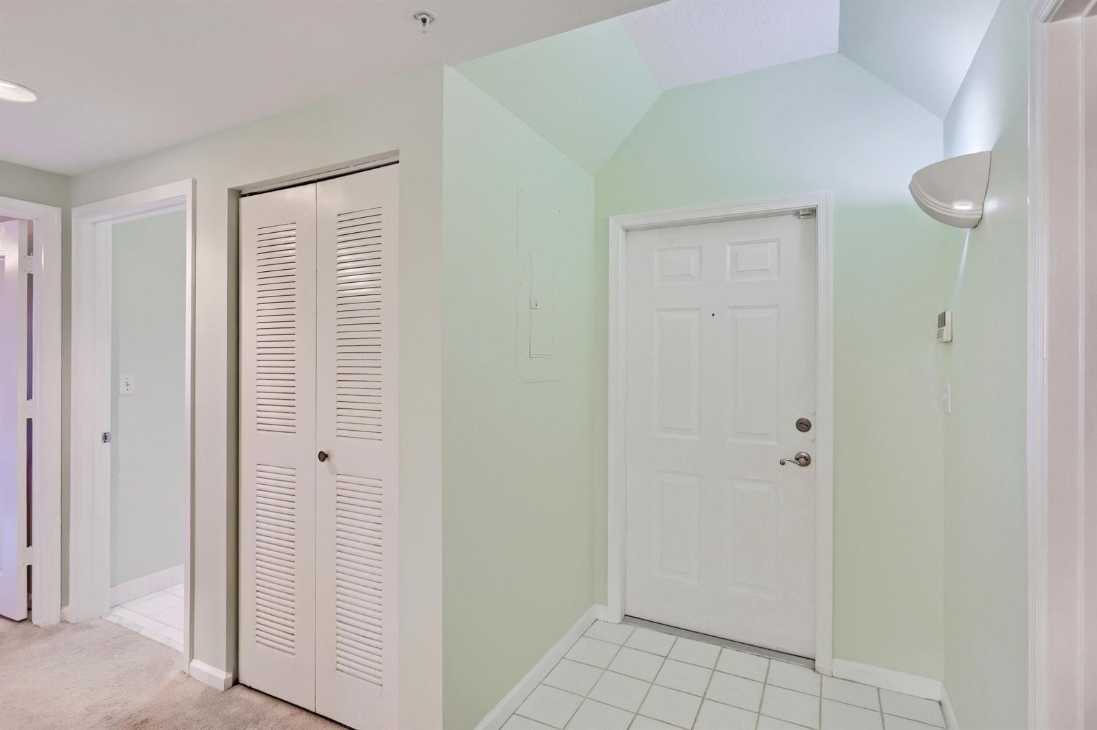 An entryway with a white door, louvered closet, tiled floor, and light green walls — 800 Uno Lago Drive # 305, Juno Beach FL 33408, JUNO BEACH, FL