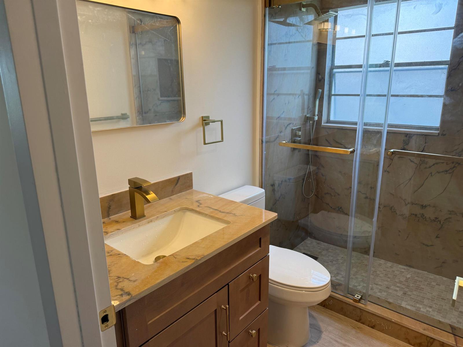 A bathroom features a wood vanity with a stone countertop, gold fixtures, and a glass shower — 47 Preston B # 47, Boca Raton FL 33434, BOCA RATON, FL