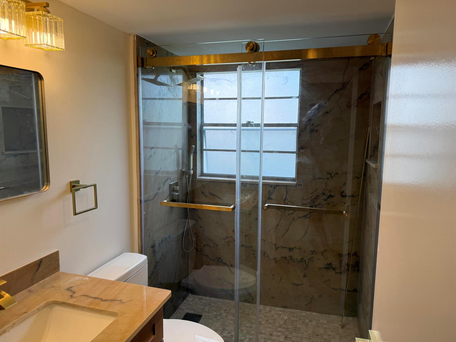 A bathroom features a walk-in shower with glass doors, gold hardware, and marble-patterned tile walls — 47 Preston B # 47, Boca Raton FL 33434, BOCA RATON, FL