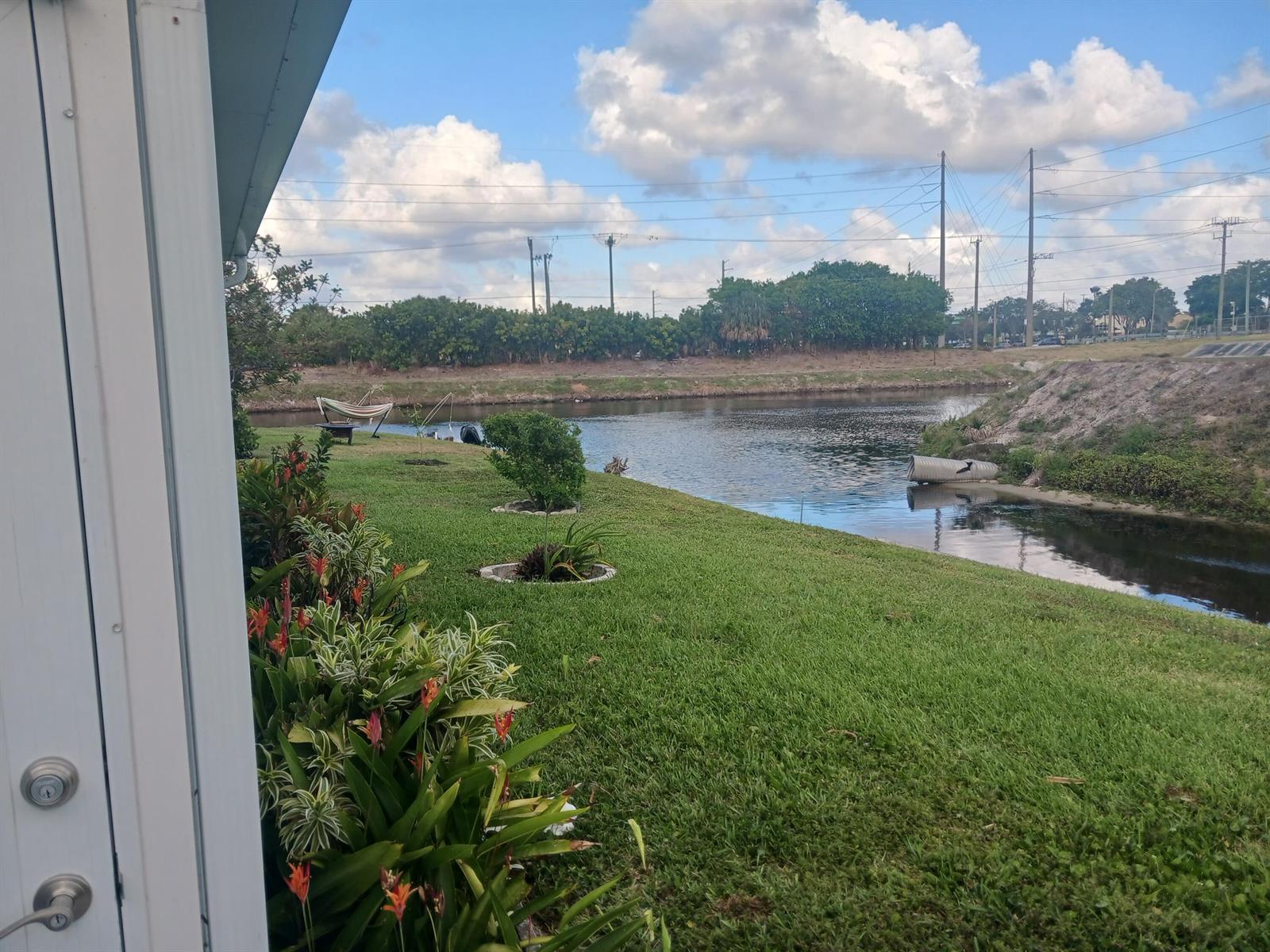 A view from a doorway overlooking a grassy backyard with a canal and power lines — 1590 SW 14th Avenue, Boynton Beach FL 33426, BOYNTON BEACH, FL
