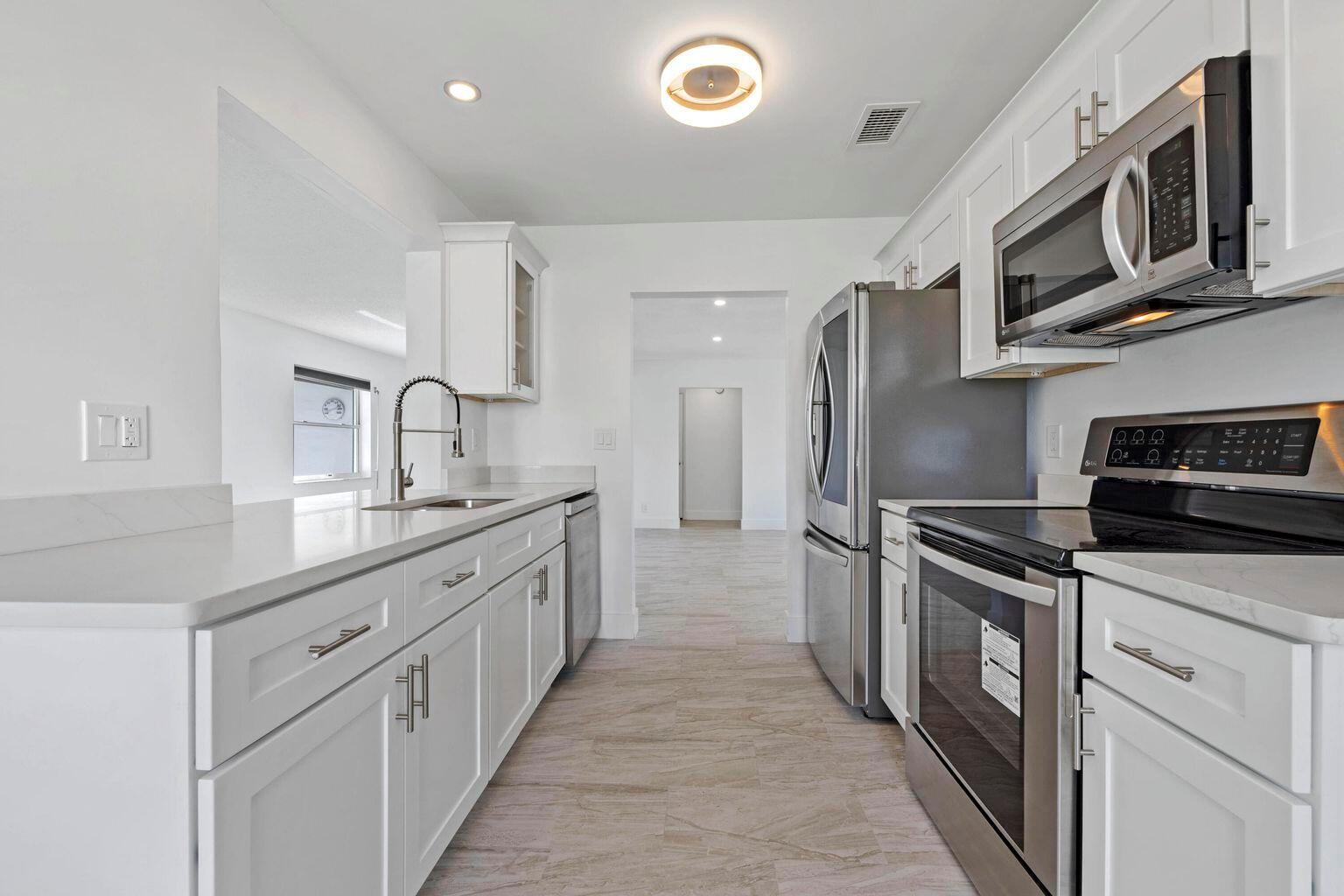 A modern kitchen features white cabinets, stainless steel appliances, and light-colored tile flooring — 1590 SW 14th Avenue, Boynton Beach FL 33426, BOYNTON BEACH, FL