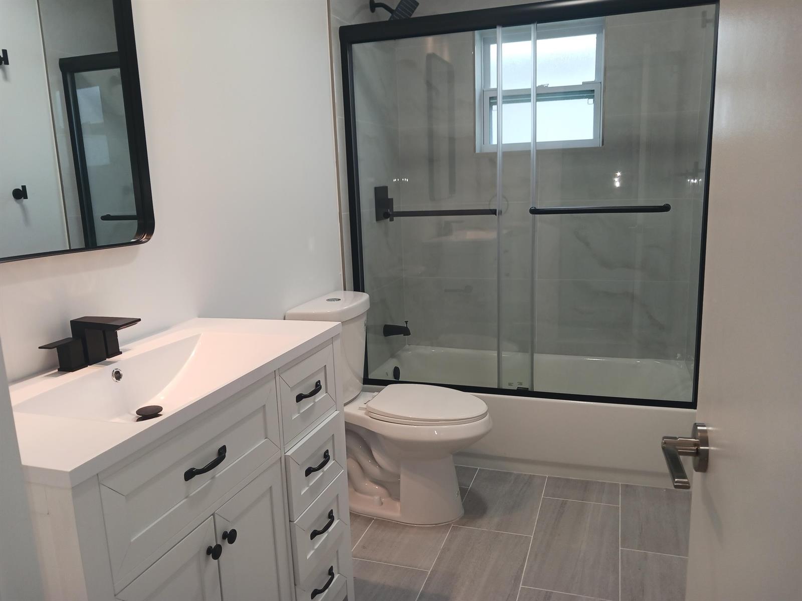 A modern bathroom features a white vanity, a toilet, and a glass-enclosed bathtub shower — 1590 SW 14th Avenue, Boynton Beach FL 33426, BOYNTON BEACH, FL