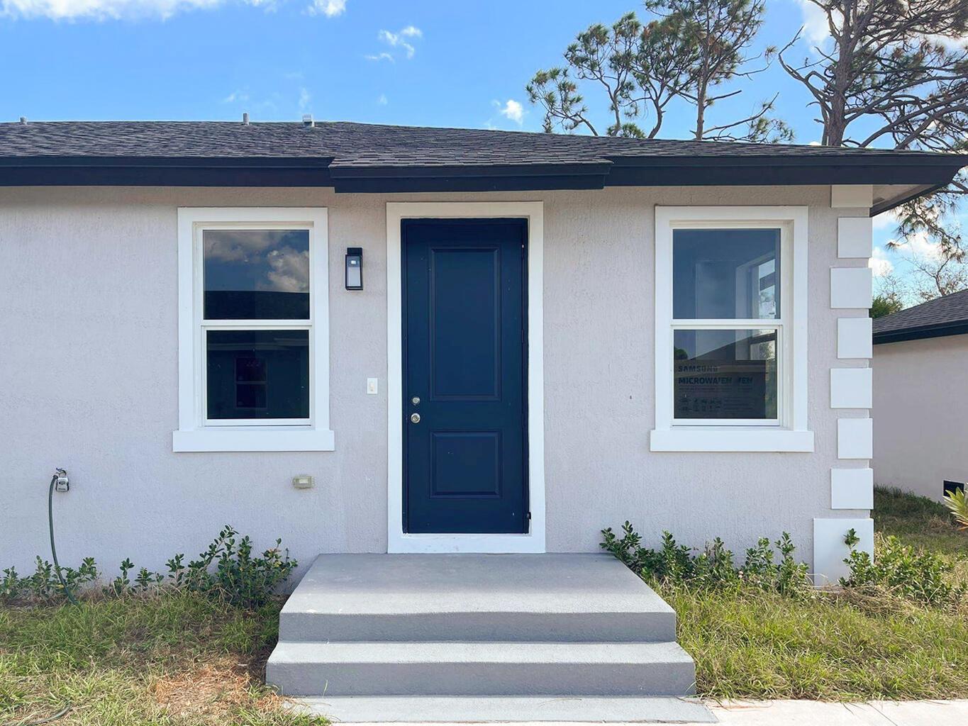 A light gray house exterior features a dark blue front door and two white-framed windows — 246 Rotonda Blvd Boulevard W # B, FL 33947, FL