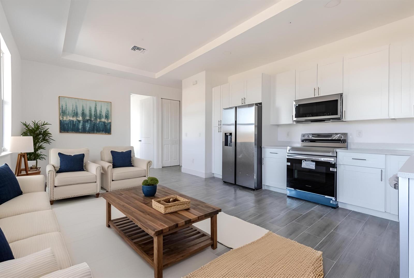 An open-concept living room and kitchen featuring white cabinetry, stainless steel appliances, and tile flooring — 246 Rotonda Blvd Boulevard W # B, FL 33947, FL