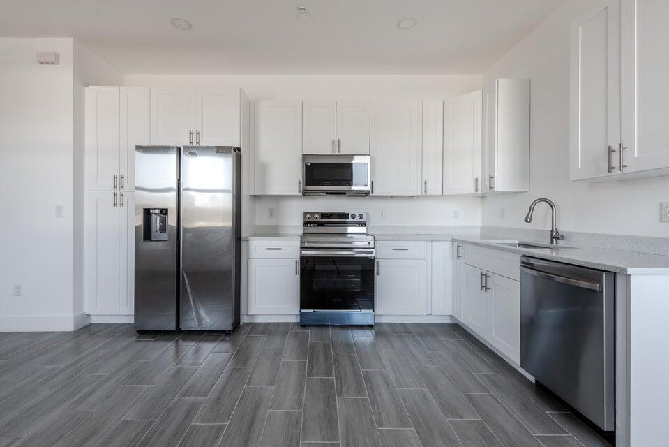A modern kitchen features white cabinetry, stainless steel appliances, and gray wood-look tile flooring — 246 Rotonda Blvd Boulevard W # B, FL 33947, FL