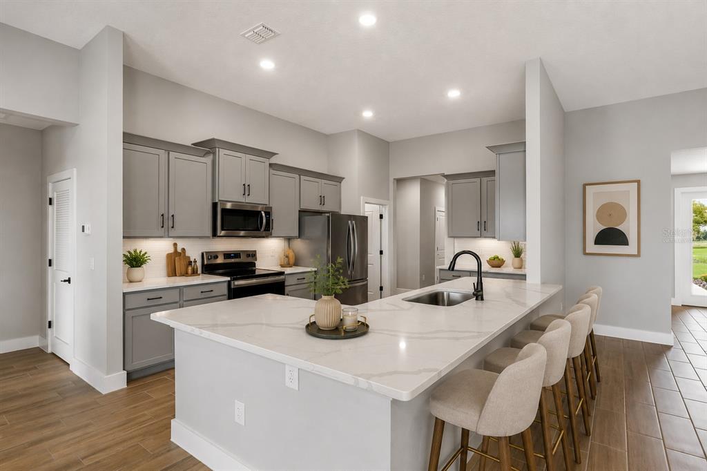A modern kitchen features gray cabinets, white quartz countertops, a large island, and wood-look flooring — 13483 LAKE GALLAGHER DRIVE, DOVER, FL