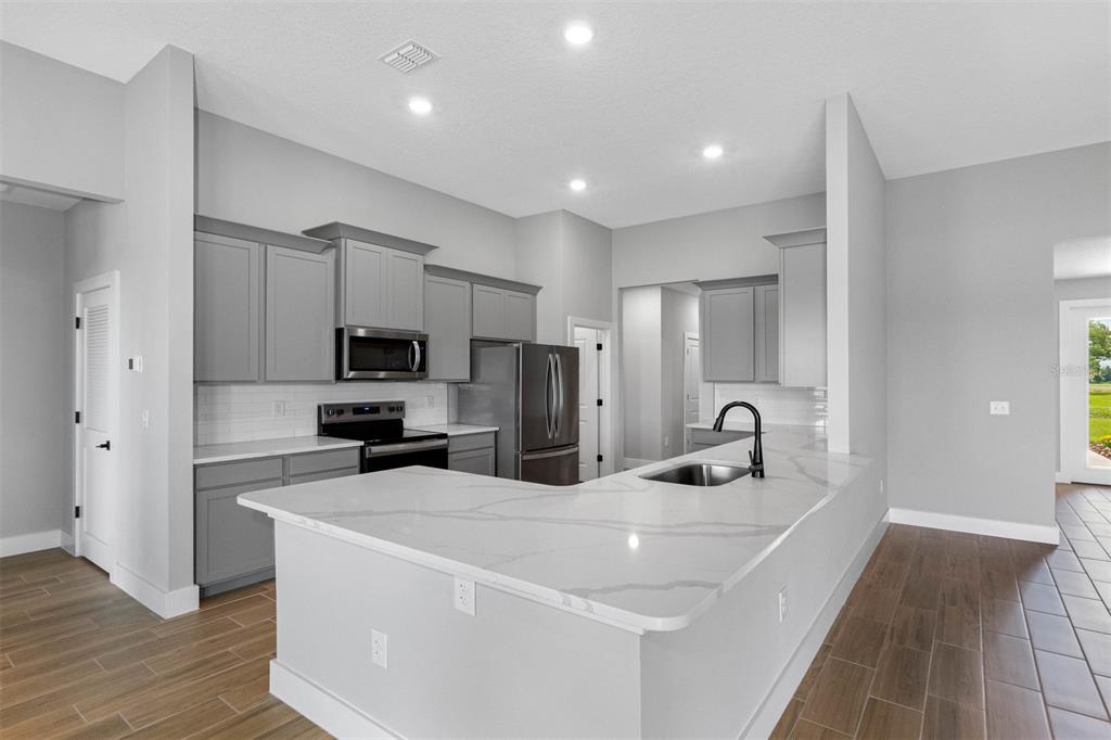 A modern kitchen features gray cabinets, white marble-look countertops, and wood-look tile flooring — 13483 LAKE GALLAGHER DRIVE, DOVER, FL
