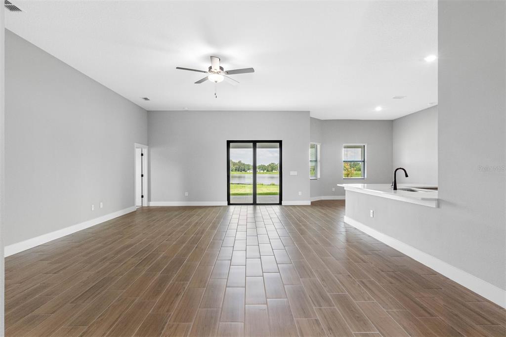 An open-concept living area with wood-look tile flooring, a ceiling fan, and sliding glass doors — 13483 LAKE GALLAGHER DRIVE, DOVER, FL