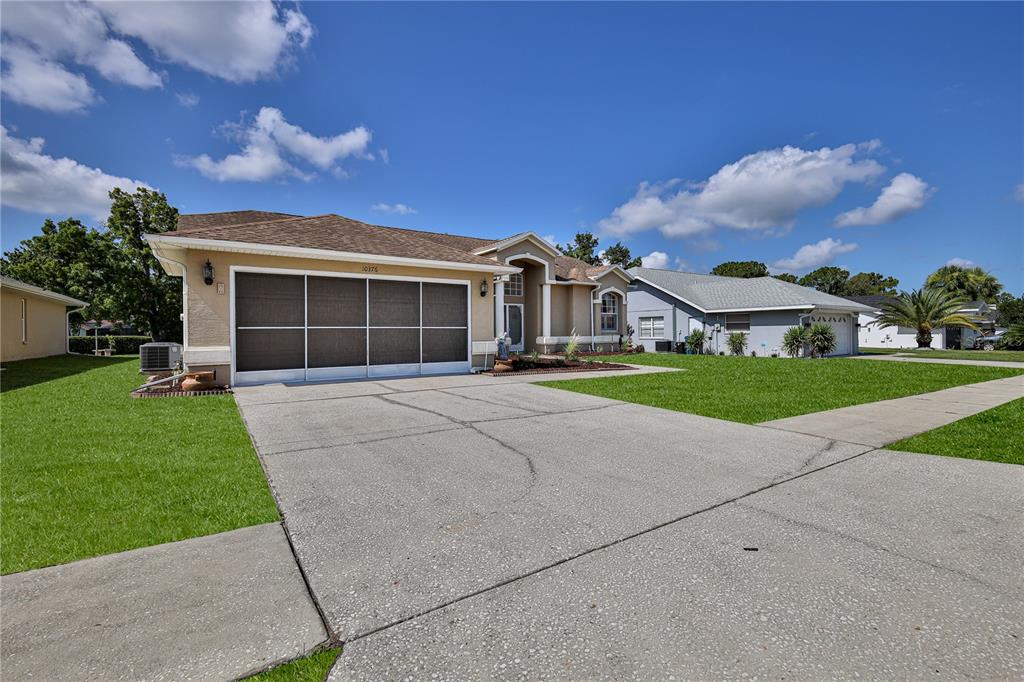 A single-story suburban house with a concrete driveway and a screened-in garage door — 10376 HENDERSON STREET, SPRING HILL, FL