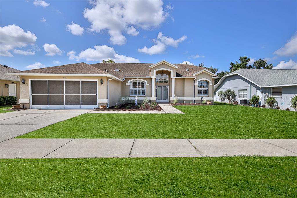 A single-story suburban house with a screened garage door, stucco exterior, and a front lawn — 10376 HENDERSON STREET, SPRING HILL, FL