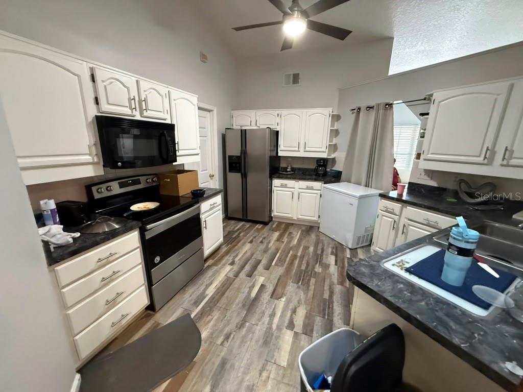 A kitchen features white cabinets, stainless steel appliances, dark countertops, and wood-look flooring — 601 S DEAN ROAD, ORLANDO, FL