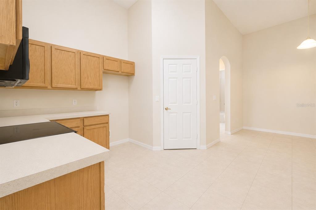 A kitchen with light oak cabinets, white countertops, and tile flooring leads to an arched doorway — 2509 LAUREL BLOSSOM CIRCLE, OCOEE, FL