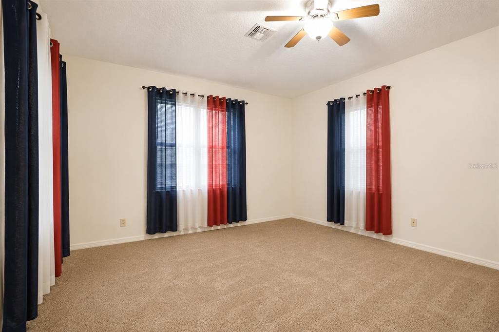 An empty bedroom features beige carpeting, white walls, a ceiling fan, and red-and-blue curtains — 2509 LAUREL BLOSSOM CIRCLE, OCOEE, FL
