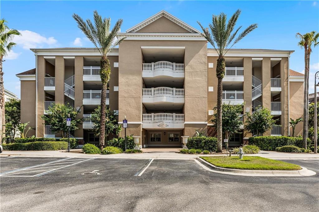 A multi-story tan apartment building features white balconies and palm trees in front — 1106 SUNSET VIEW CIRCLE UNIT 304, REUNION, FL