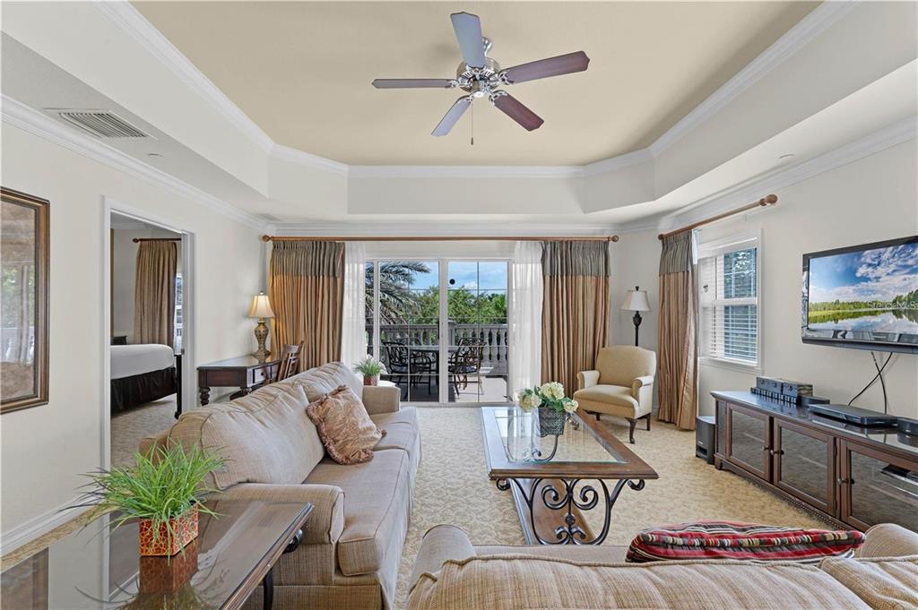 A living room with a tray ceiling, ceiling fan, beige carpet, and sliding glass balcony doors — 1106 SUNSET VIEW CIRCLE UNIT 304, REUNION, FL