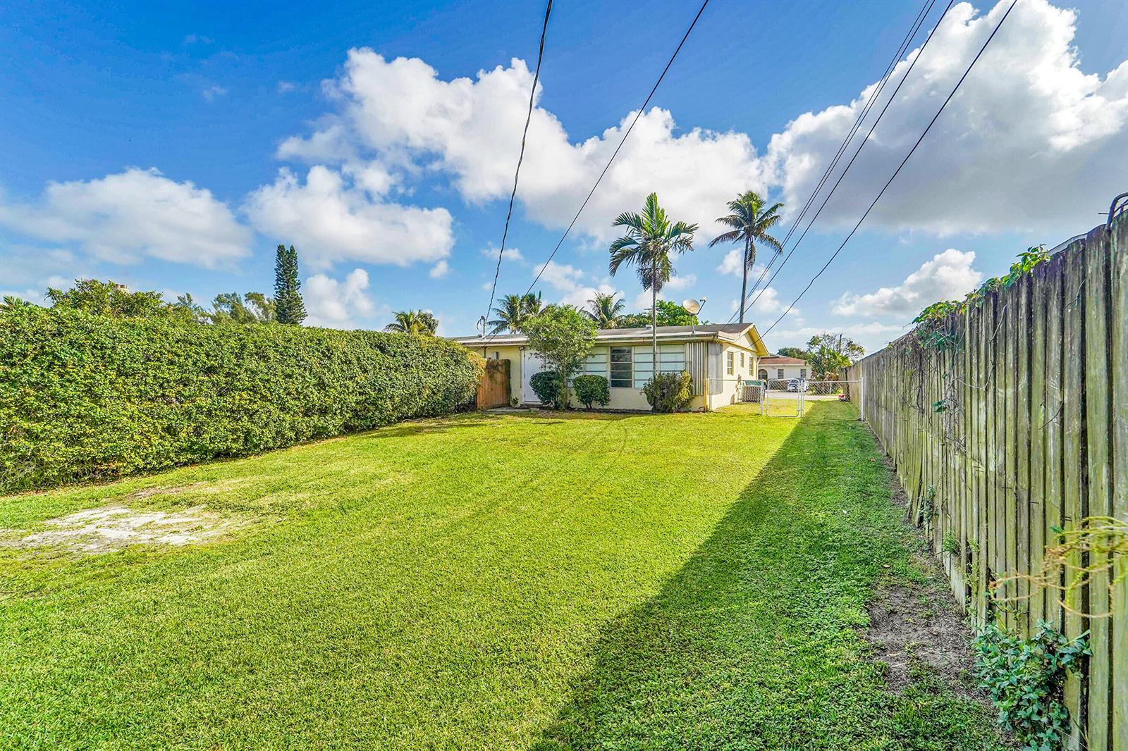 A grassy backyard features a tall hedge, a wooden fence, and a single-story house — 4681 SW 43rd Terrace # 2, Dania Beach FL 33314, DANIA BEACH, FL