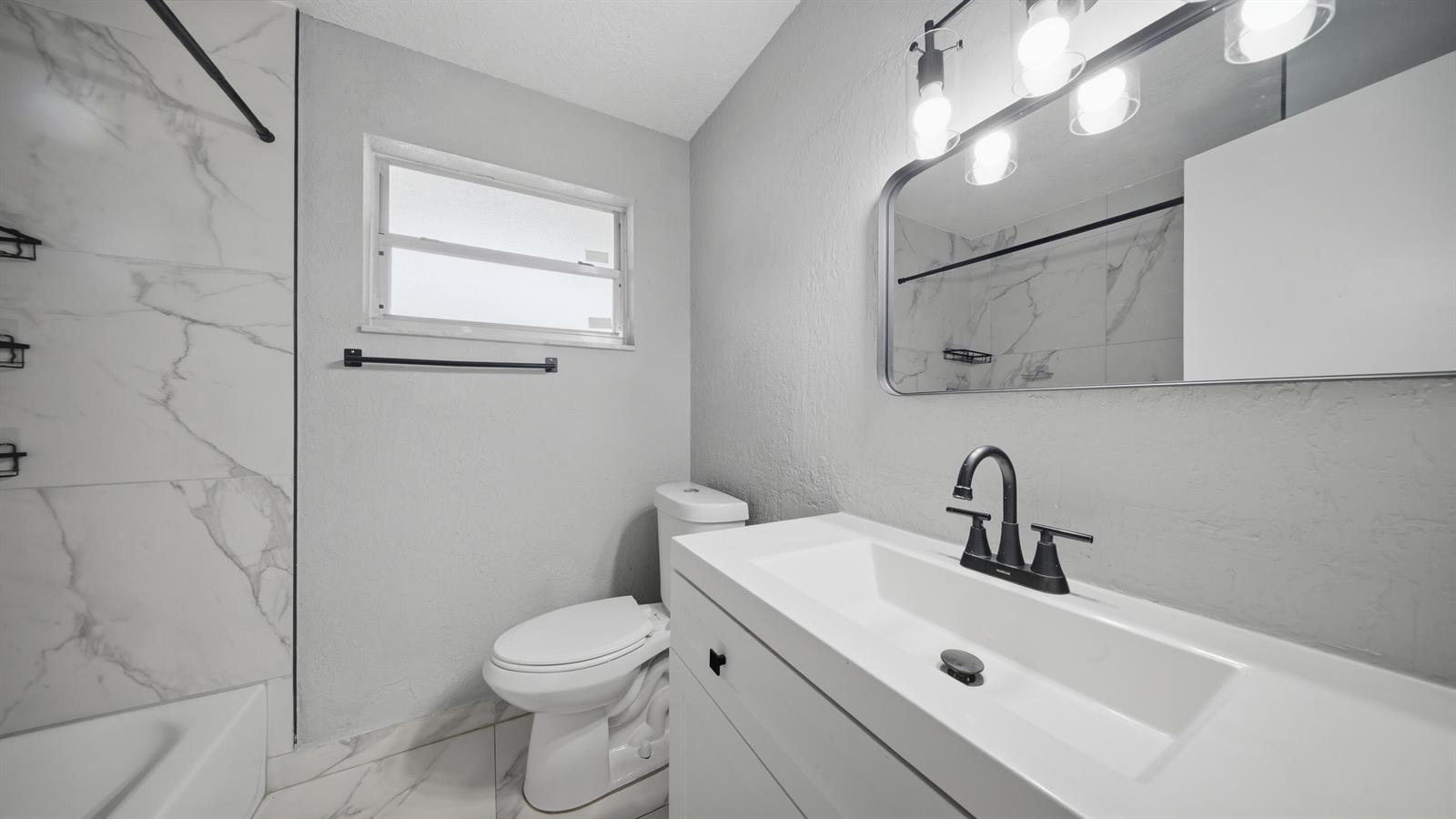 A bathroom features a white vanity with a black faucet, a toilet, and marble-look tile — 4681 SW 43rd Terrace # 2, Dania Beach FL 33314, DANIA BEACH, FL