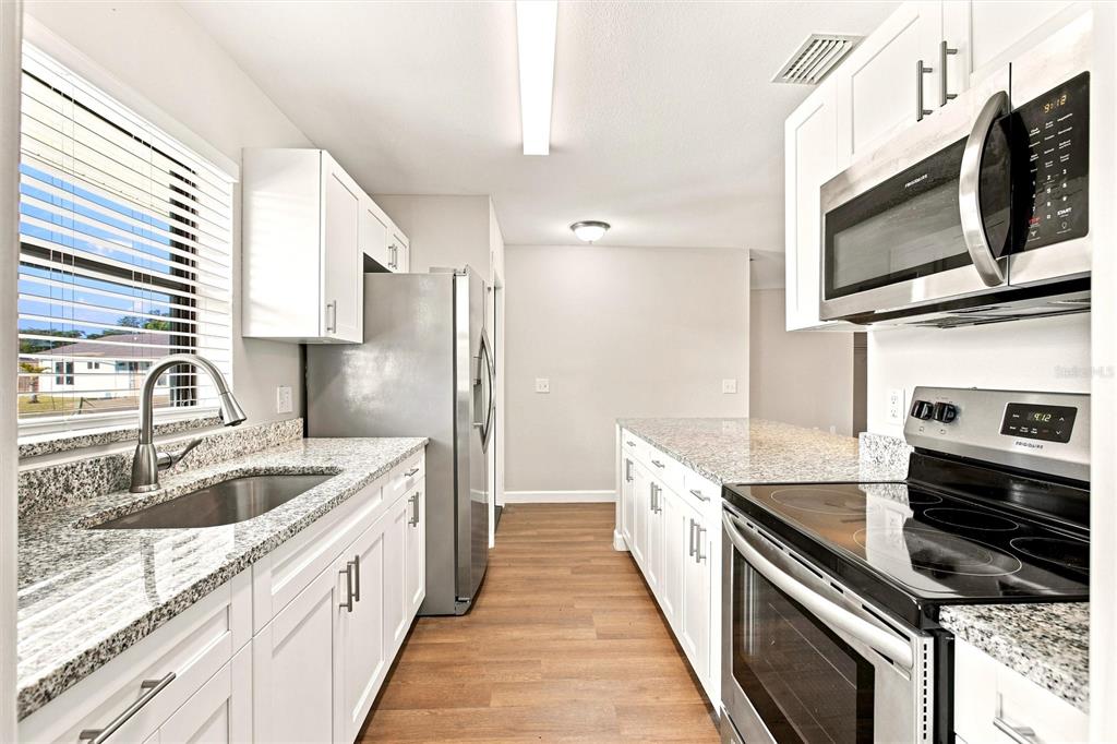 A kitchen features white cabinets, granite countertops, stainless steel appliances, and wood-look flooring — 5799 FRAN COURT, NORTH PORT, FL