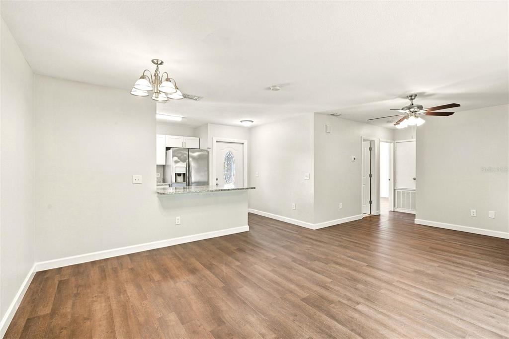 An open-concept living area features wood-look flooring, a kitchen with a breakfast bar, and ceiling fans — 5799 FRAN COURT, NORTH PORT, FL
