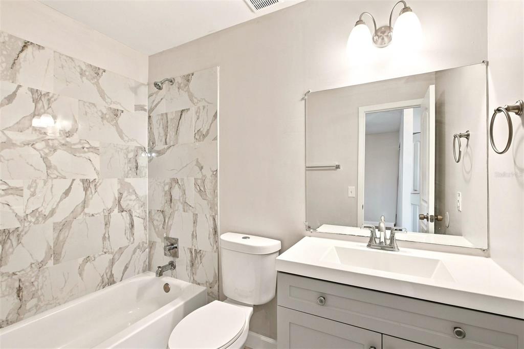A bathroom features a gray vanity, a white toilet, and a marble-tiled shower-tub combination — 5799 FRAN COURT, NORTH PORT, FL