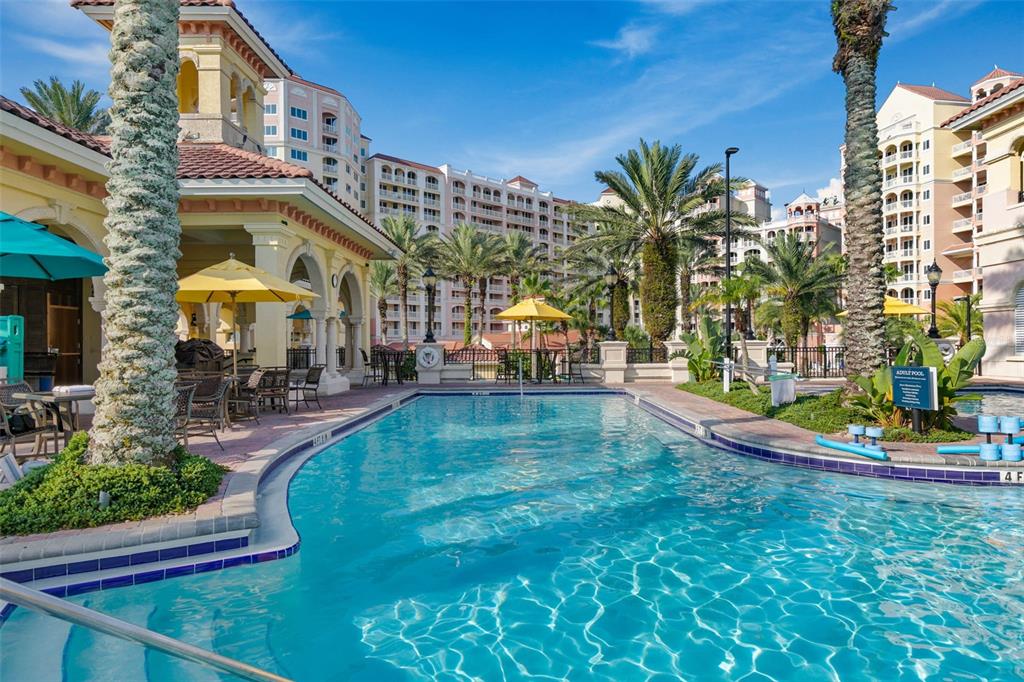 A swimming pool sits in front of a large resort building with palm trees — 200 OCEAN CREST DRIVE UNIT 913, PALM COAST, FL