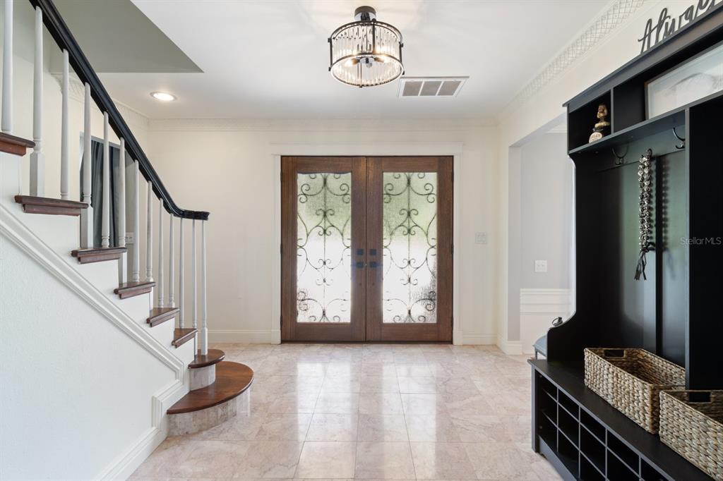 A foyer features a staircase with a dark railing, double glass doors, and tile flooring — 2065 SW 37TH STREET ROAD, OCALA, FL
