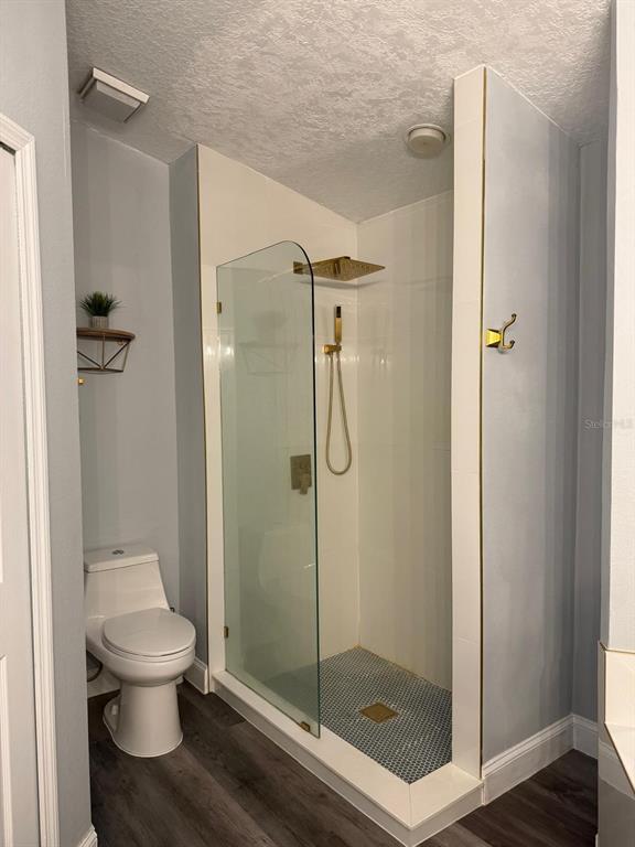 A bathroom features a walk-in shower with gold fixtures, a toilet, and wood-look flooring — 18561 3DR AVE, ORLANDO, FL