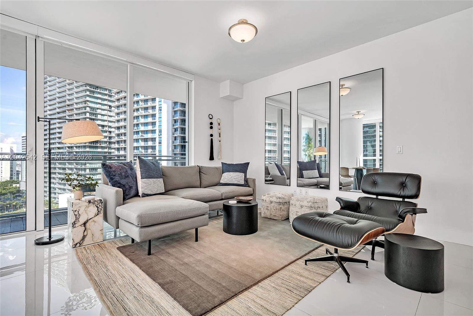 A modern living room features a gray sectional sofa, a lounge chair, and floor-to-ceiling windows — 1080 Brickell Ave # 1601, Miami FL 33131, MIAMI, FL