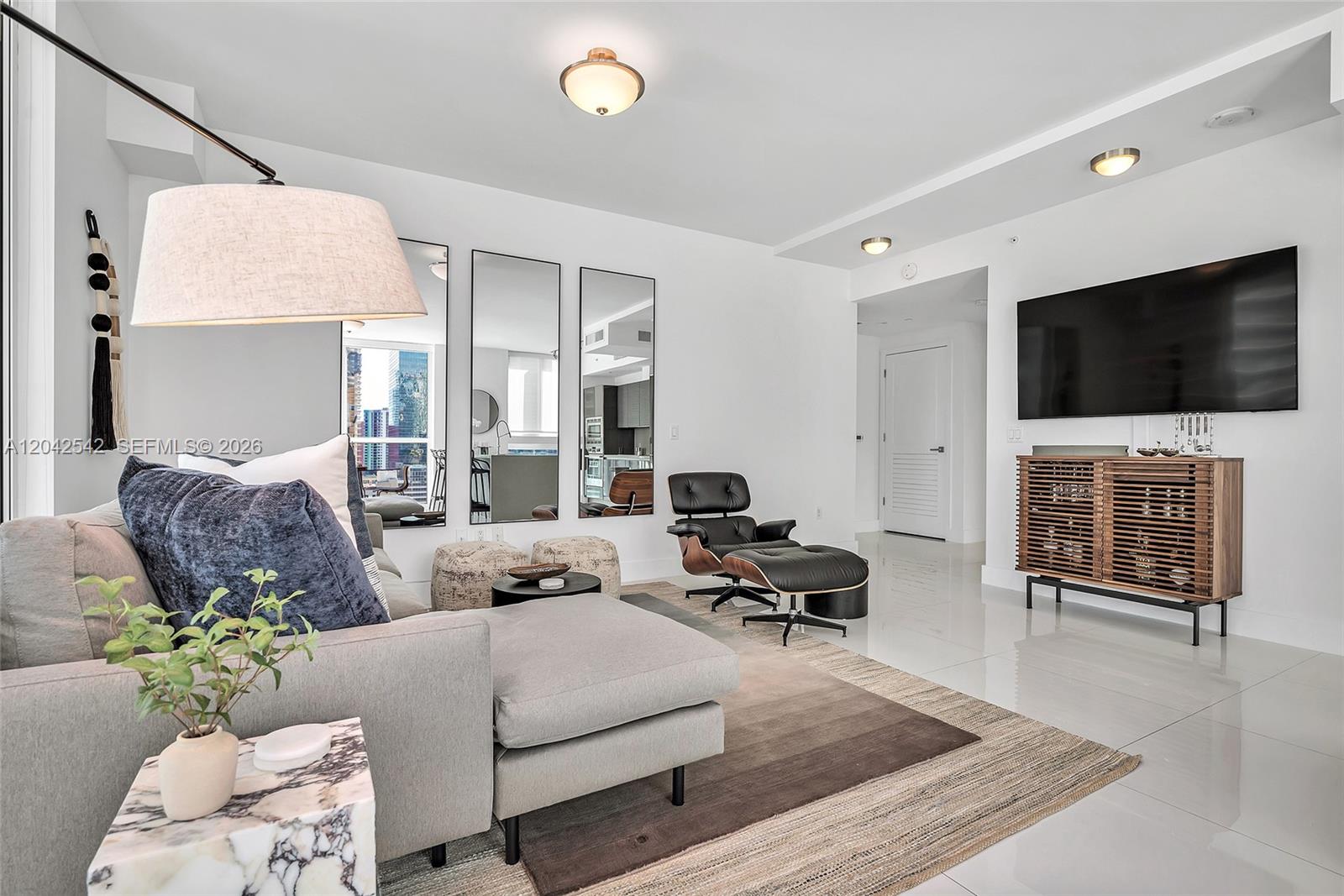 A modern living room features a sectional sofa, an Eames lounge chair, and a television — 1080 Brickell Ave # 1601, Miami FL 33131, MIAMI, FL