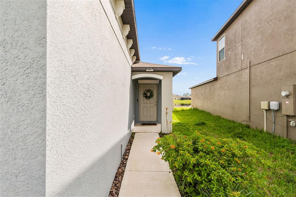 A concrete walkway leads to a front door nestled between two stucco house exterior walls — 5362 BLUE HORIZON WAY, WIMAUMA, FL