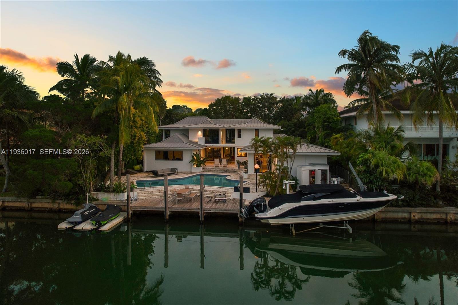 A waterfront house with a pool, wooden dock, jet skis, and a boat at sunset — 121 Knollwood Drive, Key Biscayne FL 33149, KEY BISCAYNE, FL