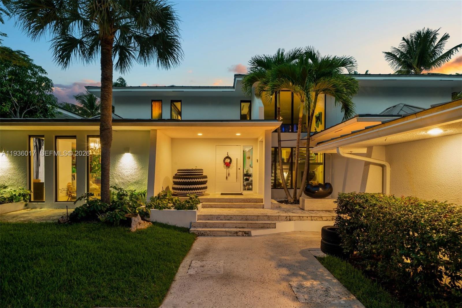 A modern two-story house exterior features a palm-lined entrance, stone steps, and warm lighting — 121 Knollwood Drive, Key Biscayne FL 33149, KEY BISCAYNE, FL