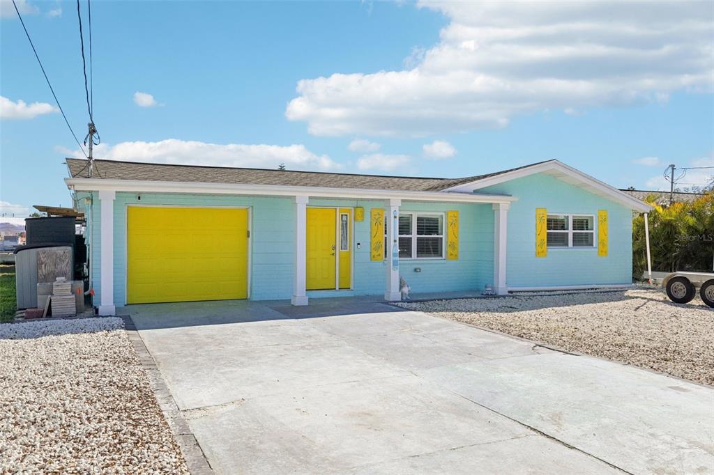 A light blue single-story house features a bright yellow garage door and front door — 13700 LESLIE DRIVE, HUDSON, FL
