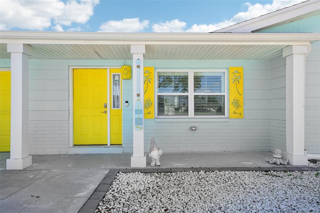 A light blue house exterior features a bright yellow door and matching decorative window shutters — 13700 LESLIE DRIVE, HUDSON, FL