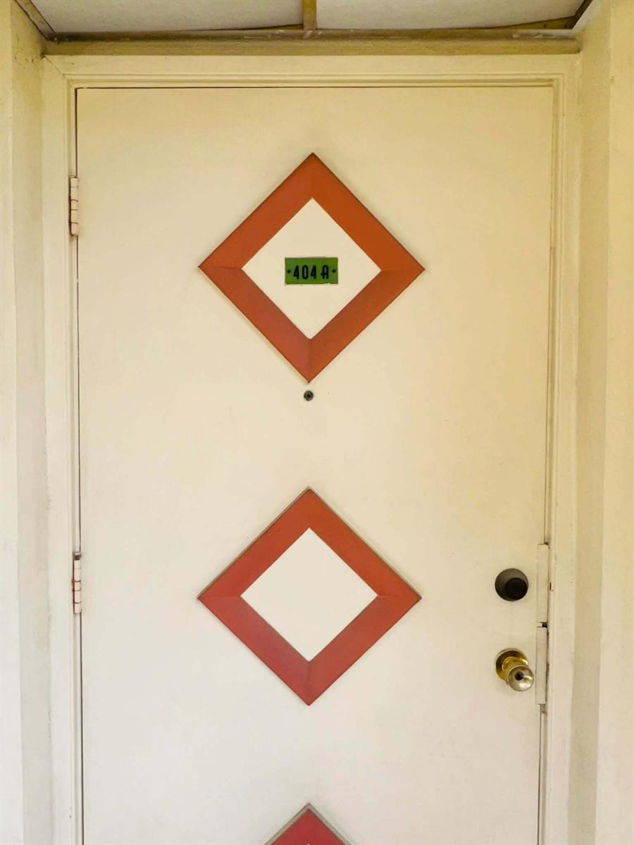 A white door features two orange diamond-shaped accents and a green unit number sign — 215 SE 3rd Avenue, Hallandale Beach FL 33009, HALLANDALE BEACH, FL