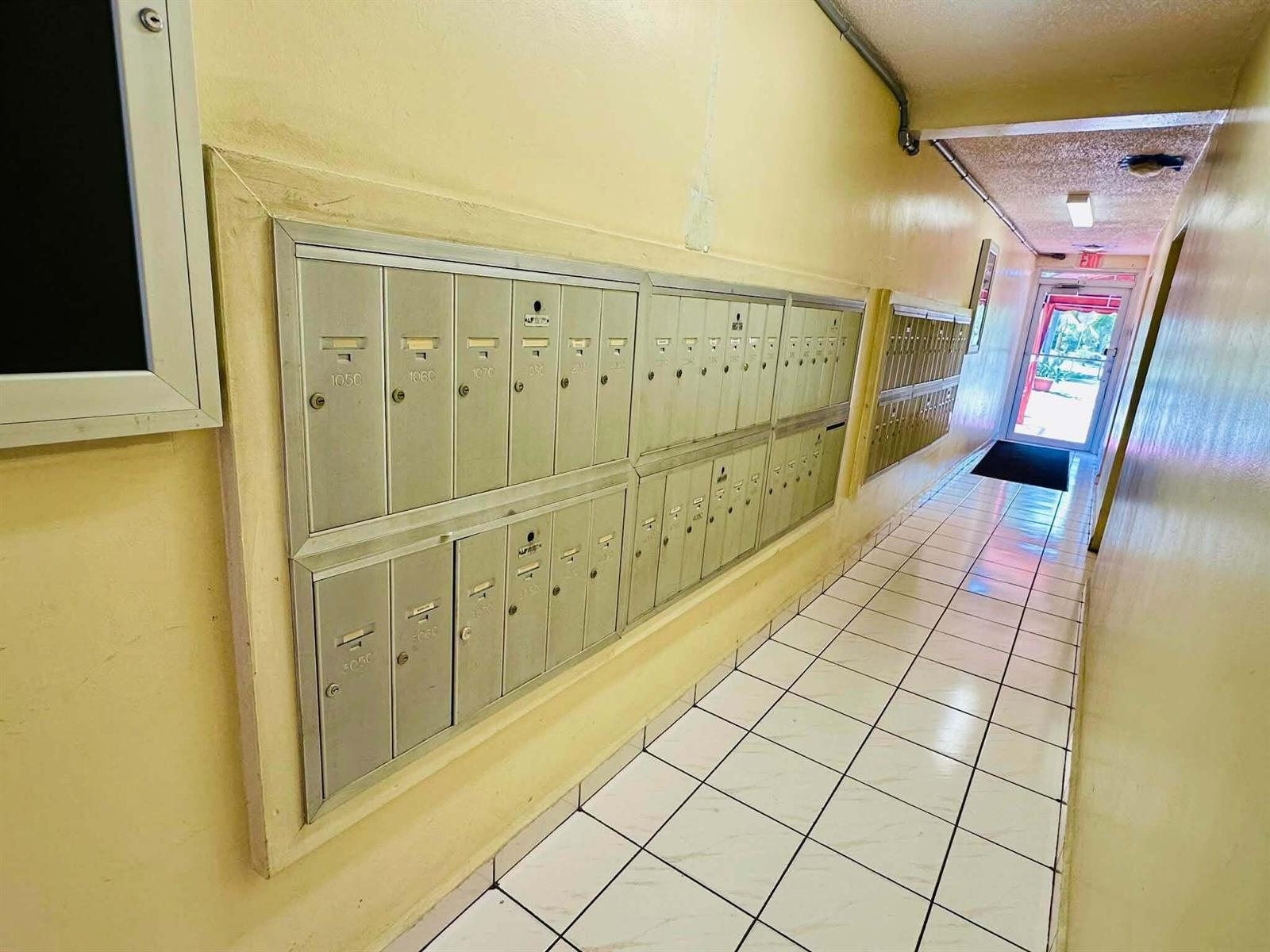 A hallway with tiled floors features a wall of metal mailboxes leading to an exit — 215 SE 3rd Avenue, Hallandale Beach FL 33009, HALLANDALE BEACH, FL