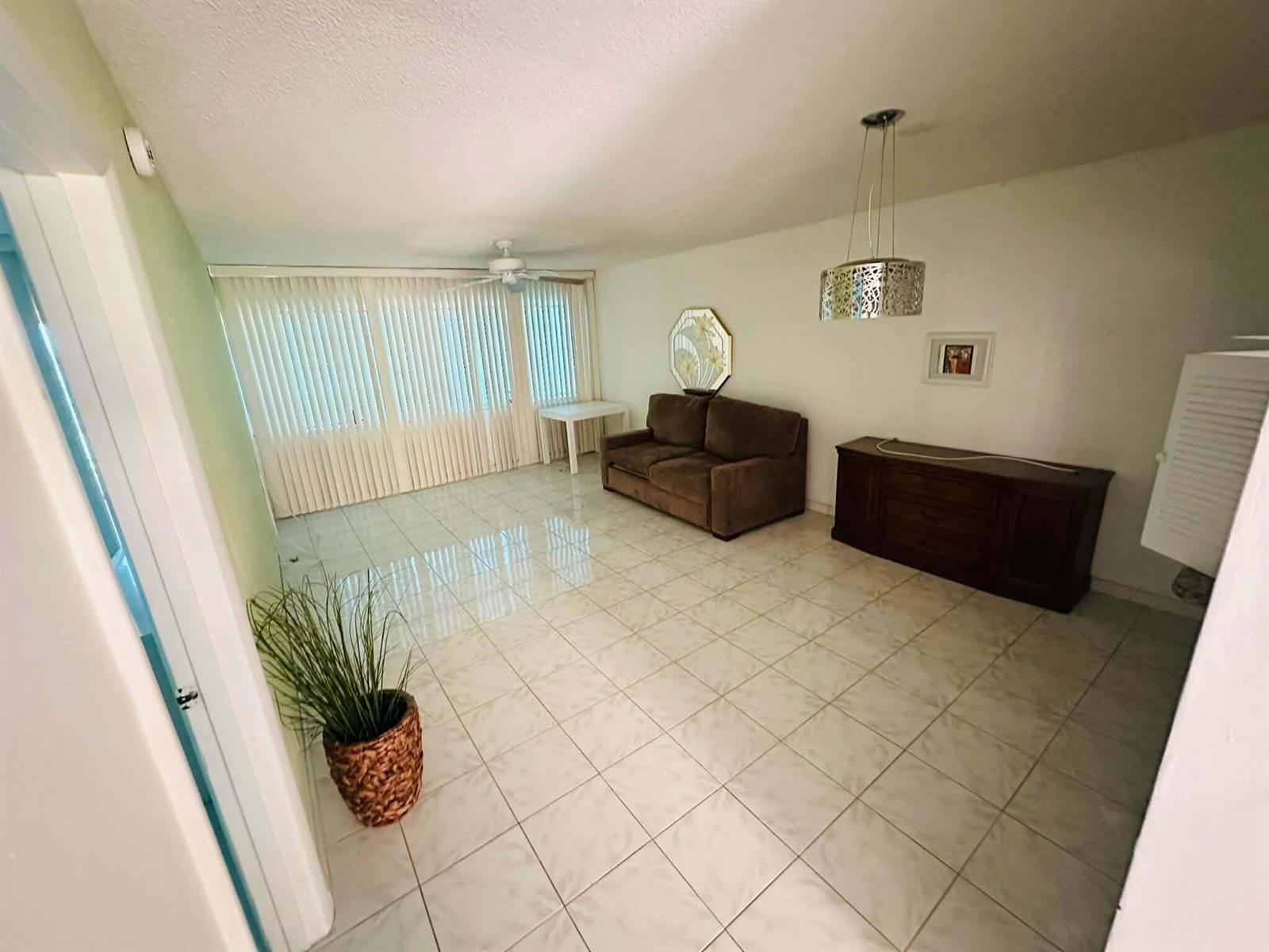 A living room features light tile flooring, a brown sofa, and a large window with blinds — 215 SE 3rd Avenue, Hallandale Beach FL 33009, HALLANDALE BEACH, FL