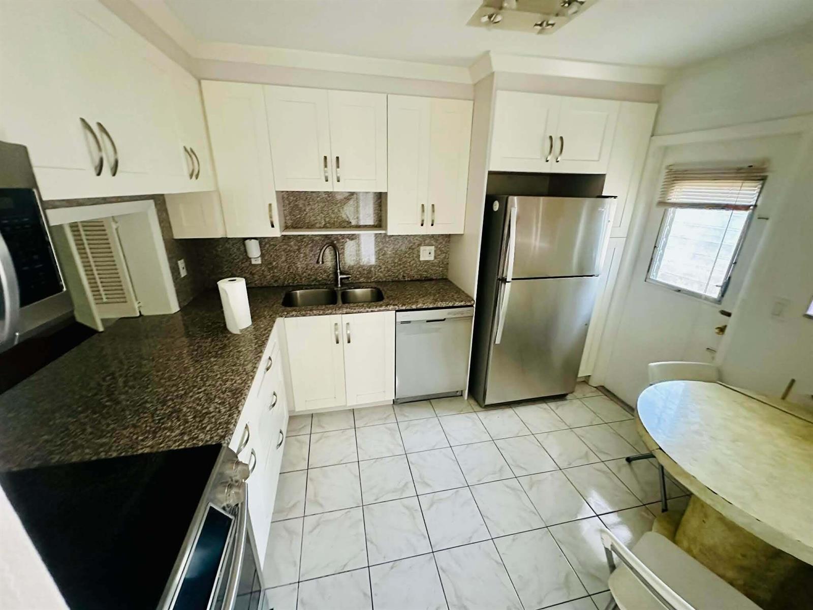 A kitchen features white cabinetry, granite countertops, stainless steel appliances, and light-colored tile flooring — 215 SE 3rd Avenue, Hallandale Beach FL 33009, HALLANDALE BEACH, FL