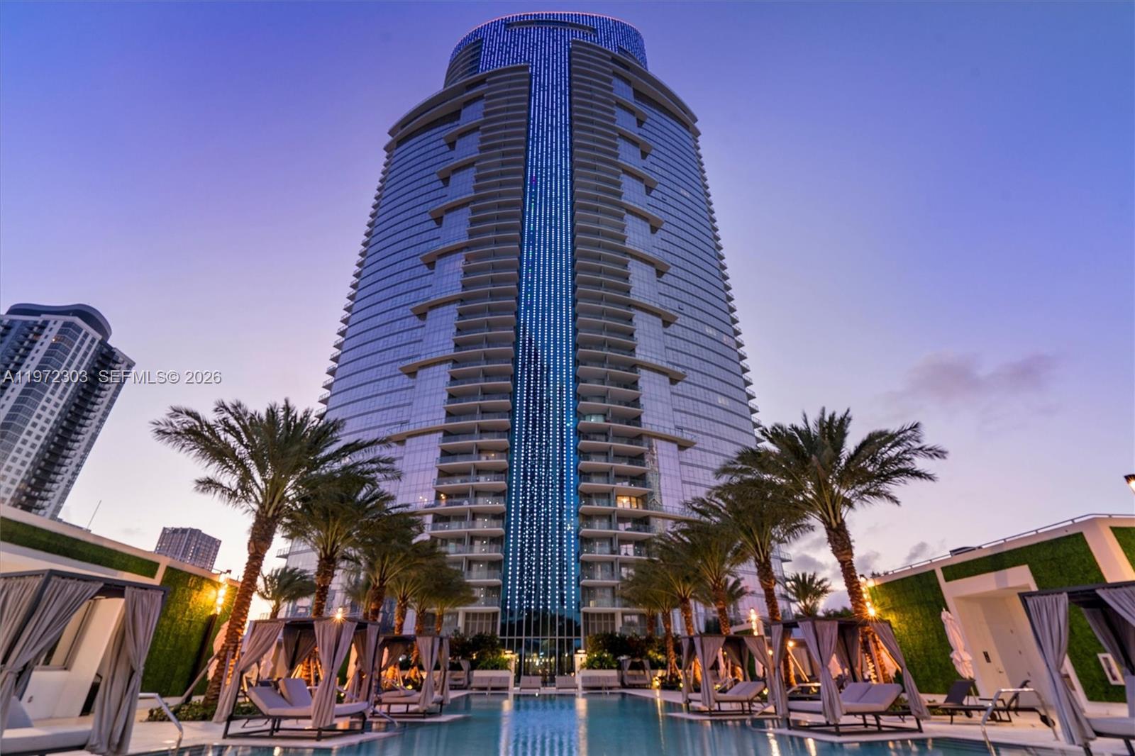 A low-angle view shows a modern glass skyscraper rising above a pool deck with cabanas — 851 NE 1st Ave # 1712, Miami FL 33132, MIAMI, FL
