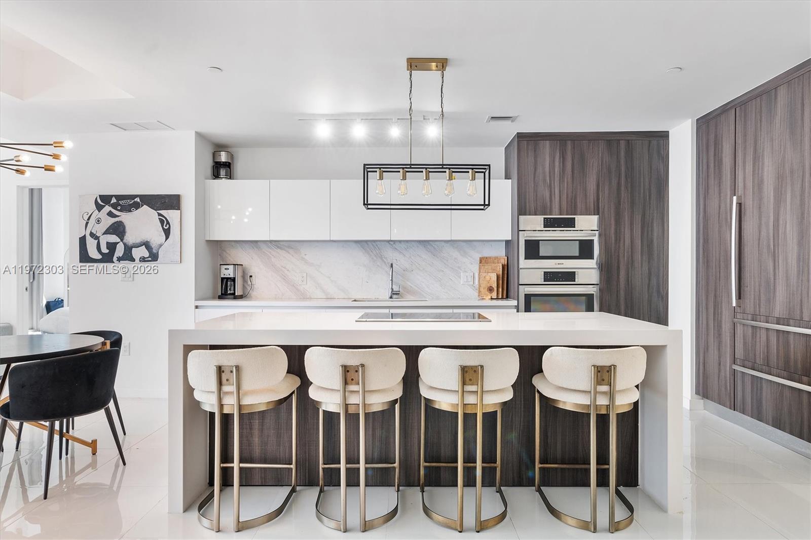 A modern kitchen features a white waterfall island with four barstools and dark wood cabinetry — 851 NE 1st Ave # 1712, Miami FL 33132, MIAMI, FL