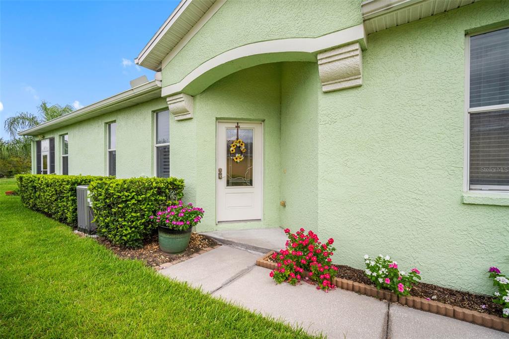 A light green stucco house exterior features a front door, walkway, and landscaped flower beds — 11588 CAPTIVA KAY DRIVE, RIVERVIEW, FL