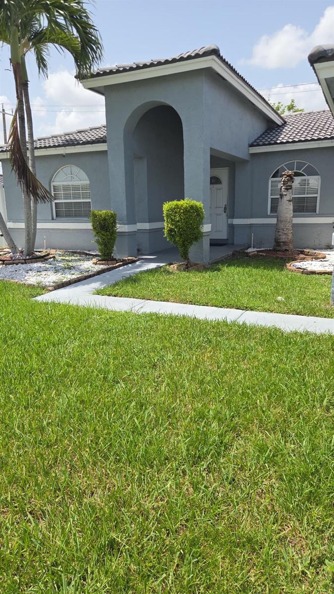 A gray single-story house with an arched entryway, white trim, and a manicured front lawn — 8221 NW 45TH Street, Lauderhill FL 33351, LAUDERHILL, FL