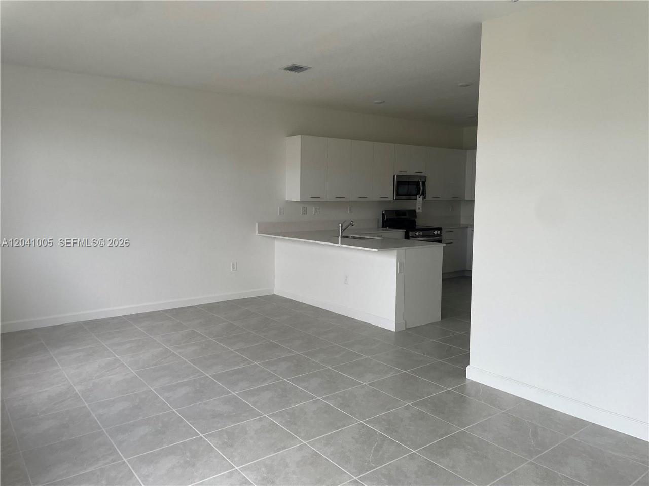 A kitchen with white cabinets and a peninsula overlooks an open-concept tiled living area — 12612 NW 22nd Pl # 12612, Miami FL 33167, MIAMI, FL