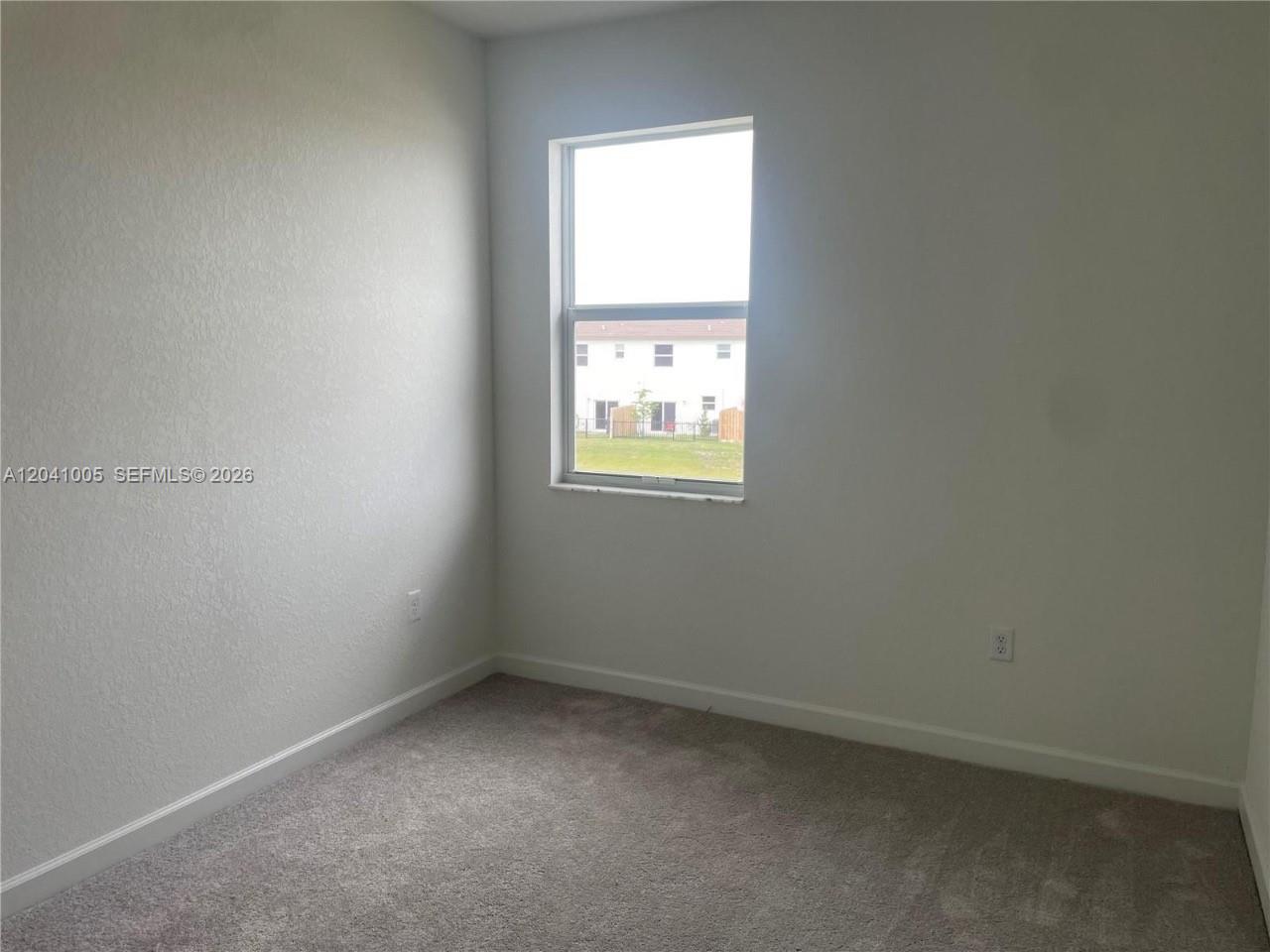 A small, empty bedroom features light gray walls, beige carpeting, and a single window — 12612 NW 22nd Pl # 12612, Miami FL 33167, MIAMI, FL